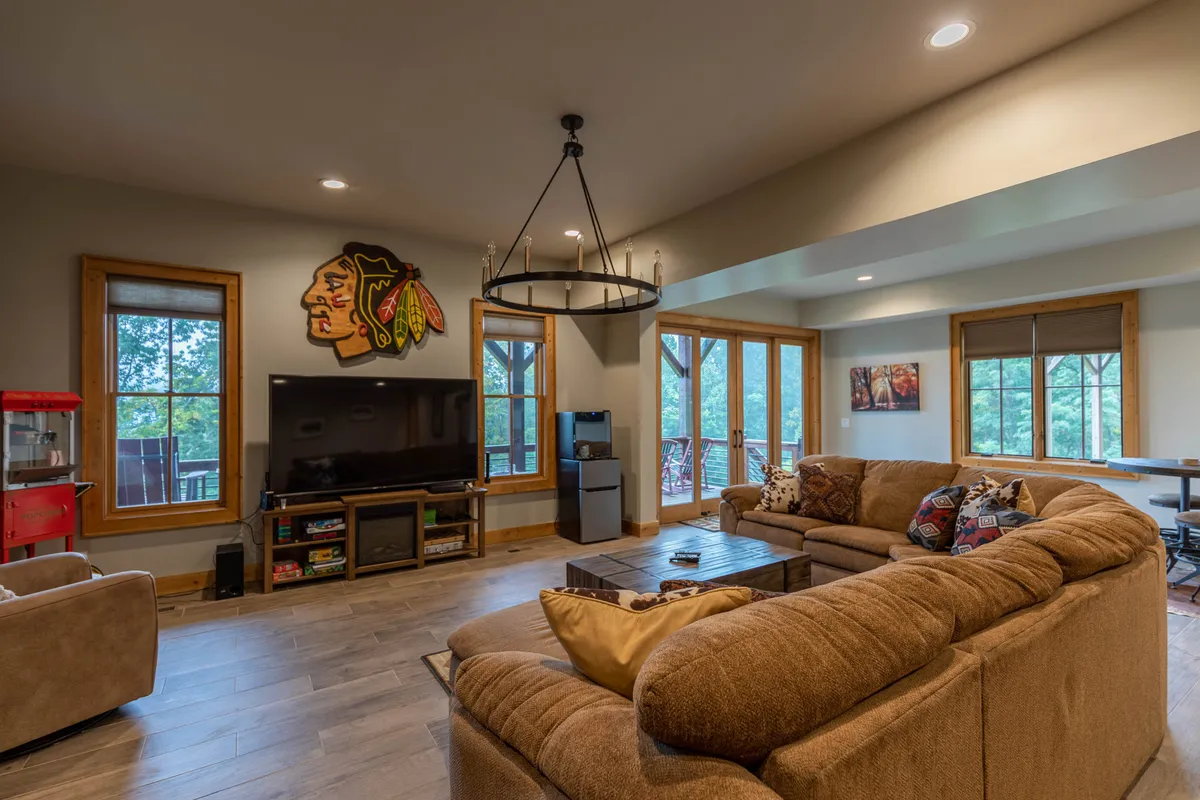 This image features a large sectional sofa facing a TV unit, with artwork on the wall and large windows allowing ample natural light into the room. The comfortable arrangement invites movie nights, socializing, and family time, all within a relaxed and cozy ambiance.