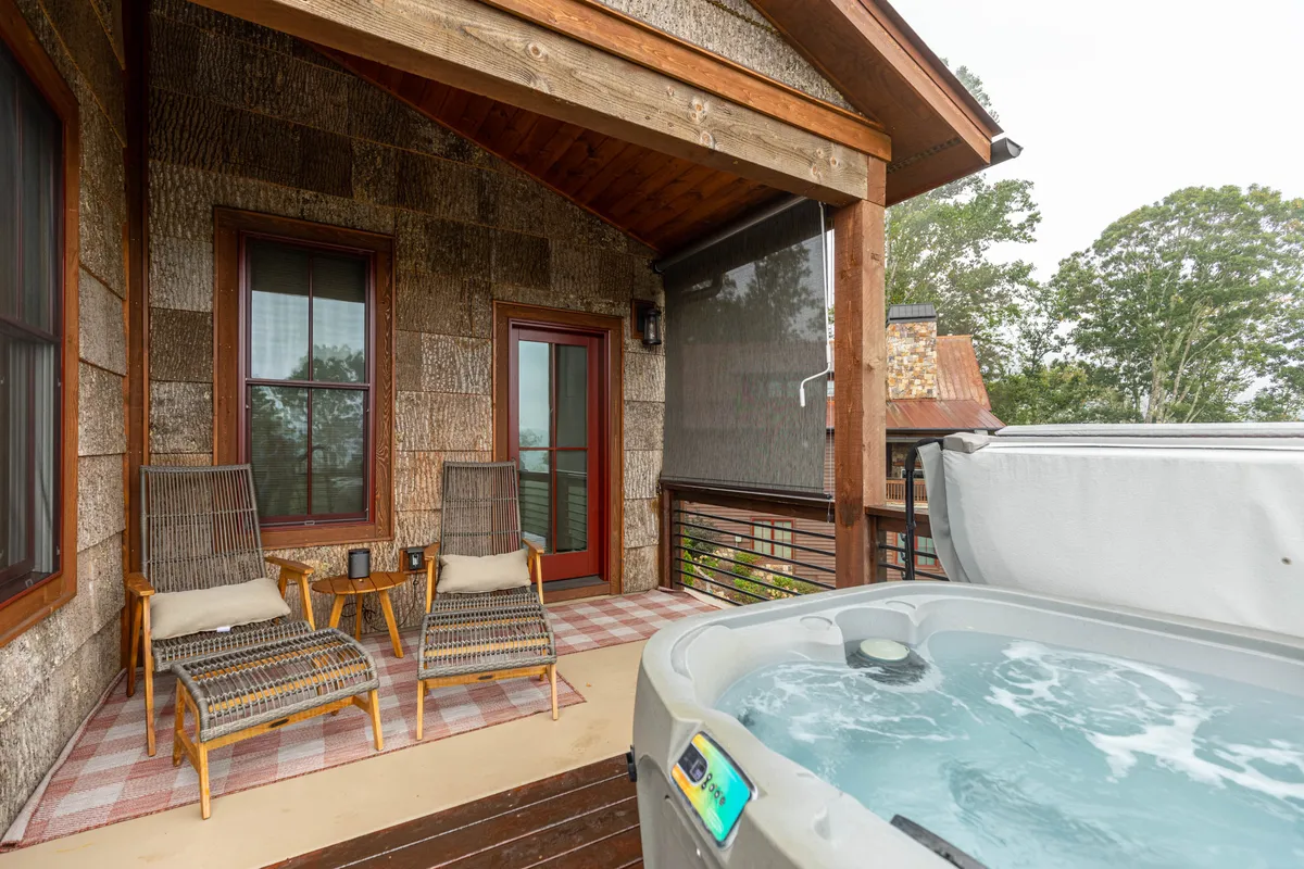 This exterior shot features a hot tub nestled on a wooden deck, surrounded by sturdy beams and a textured wall. Comfortable seating is positioned to take in the tranquil atmosphere and scenic views beyond. The setting is ideal for relaxation, whether stargazing from the warm water, sipping morning coffee, or enjoying intimate conversations at sunset.