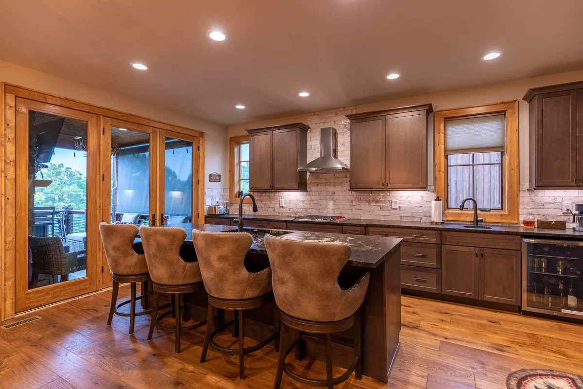 A bright, open kitchen featuring a large island with bar stools, stainless steel appliances, and sliding glass doors that hint at easy access to the outdoor deck. The layout is perfect for multiple chefs and casual gatherings, with the island serving as both a prep space and a social hub.