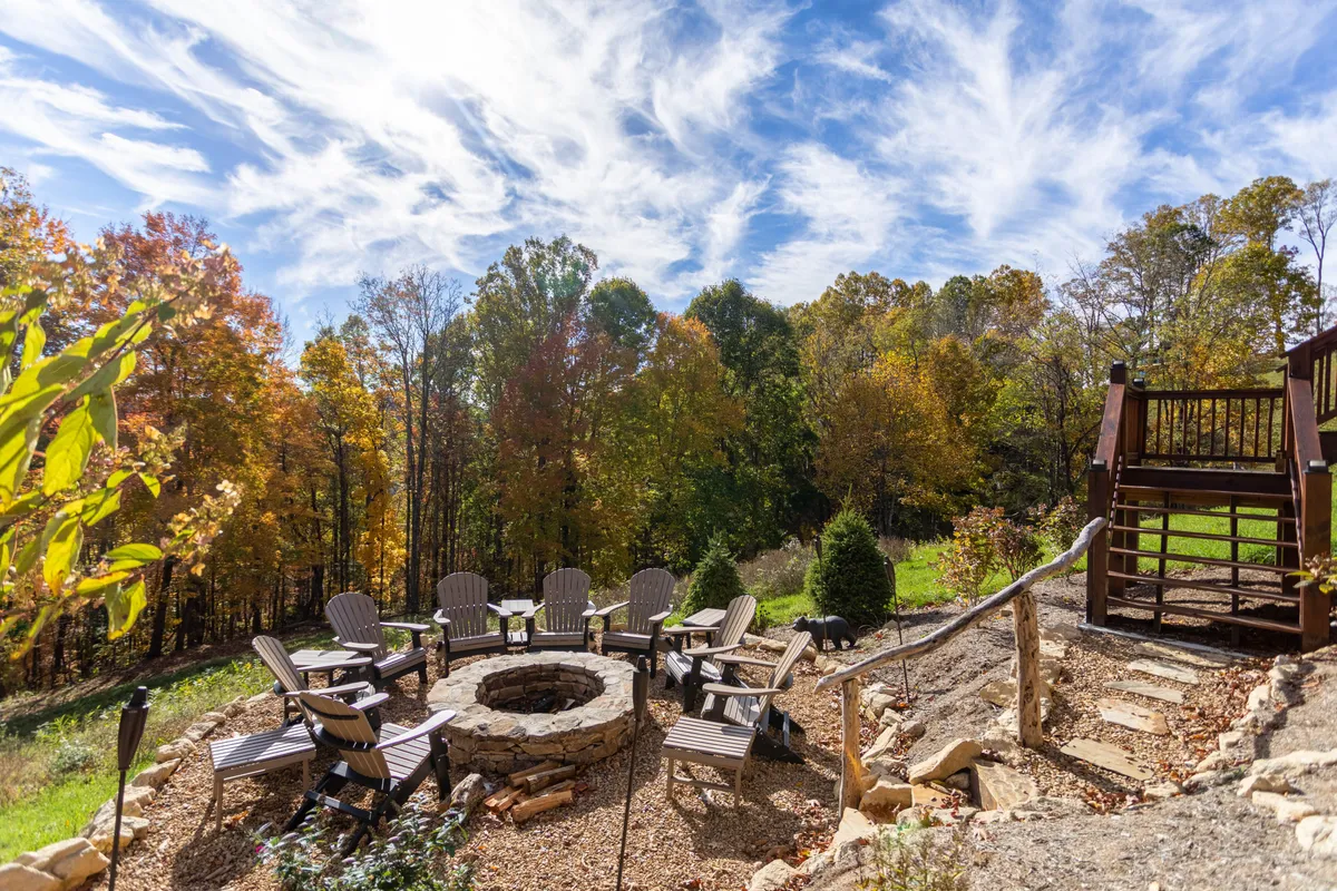 A cozy circular stone fire pit is surrounded by comfortable chairs, set amid colorful autumn trees. The area invites groups to gather for conversations, storytelling, or stargazing by the fire, with the warm glow creating a welcoming atmosphere for families and friends.