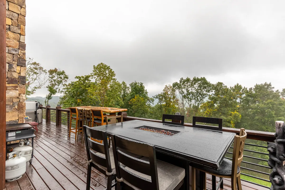 An outdoor dining table sits on a rain-soaked deck enveloped by trees, evoking a sense of intimacy and connection with nature. The space is clearly designed for enjoying the outdoors, rain or shine.