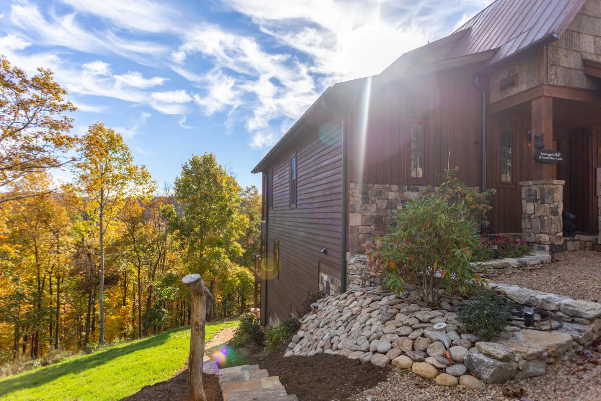 This image shows a welcoming wooden house nestled among colorful trees, with a stone pathway leading up to it. The lush surroundings and the inviting exterior suggest a serene, natural setting—perfect for outdoor exploration and family fun, including pets.