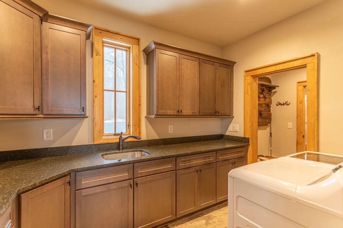 A functional corner of the home with kitchen cabinets, a sink, and a window providing natural light. The scene suggests an area where chores such as laundry or prepping supplies can take place, enhancing the practical aspects of daily living.