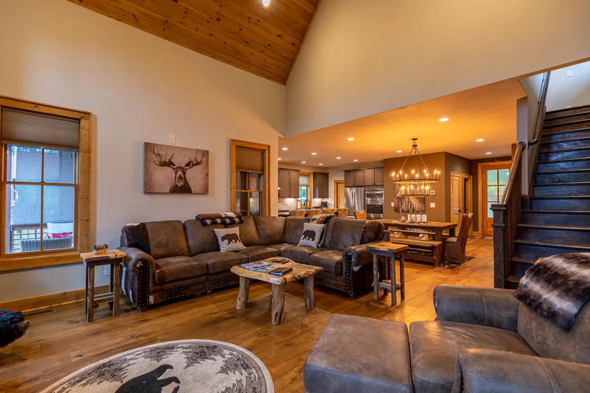 A spacious living area centered on a generous sectional sofa with a wooden coffee table and a view of the adjacent dining area. The room radiates warmth and is perfect for movie nights, storytelling, or relaxing by the fire with family and friends.