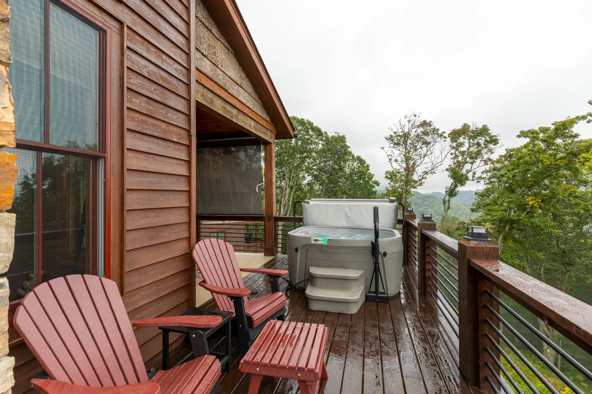 A wooden deck with an inviting hot tub and nearby Adirondack chairs, nestled against a lush wooded backdrop. The spot offers tranquil views for relaxing after a day of activities, perfect for stargazing or enjoying the peaceful sounds of nature.