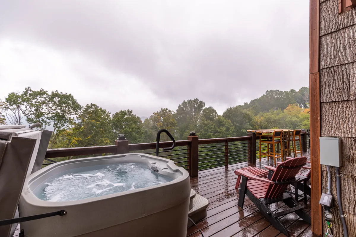 An inviting outdoor deck connected to one of the bedrooms, featuring a hot tub, Adirondack chairs, and expansive scenic views, perfect for morning coffee or stargazing.