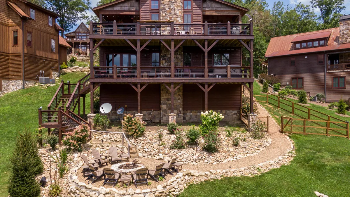 This image highlights the three-story wooden house, a well-landscaped garden, a stone patio with a fire pit area, and plenty of space for families or friends to spread out. The balcony offers panoramic sunset views, and the fire pit area is ideal for evening group activities.