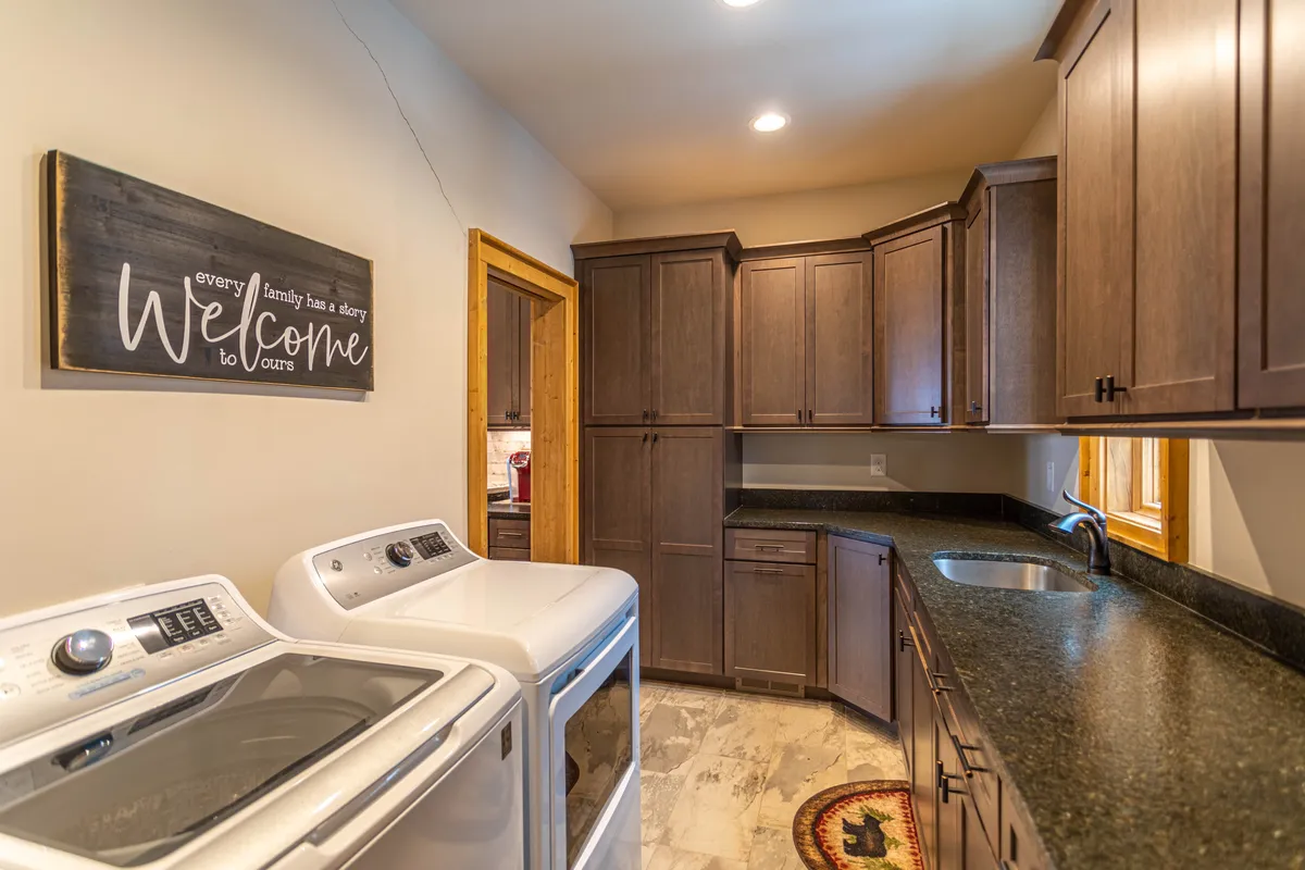 A well-lit laundry room featuring a modern washing machine and drying machine, complemented by dark wood cabinetry and a utility sink. The space is organized and inviting, suitable for handling family laundry days or cleaning up after outdoor adventures.